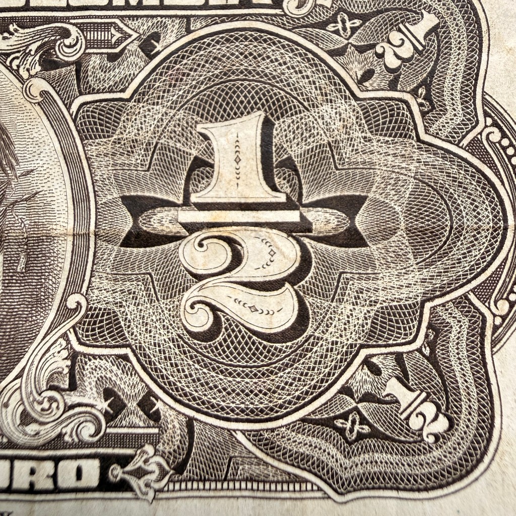 Close-up detail of the number “½” on a vintage Colombian half peso banknote, showing intricate engraved linework, ornamental patterns, and fine guilloché texture.